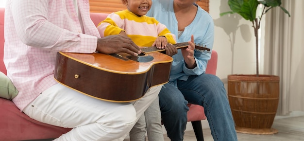 Happy family playing guitar together on the couch in living room at home