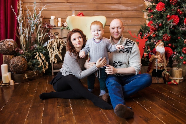 Happy family portrait on Christmas, mother, father and son sitting on highchair at home, chritmas decoration and presents around them