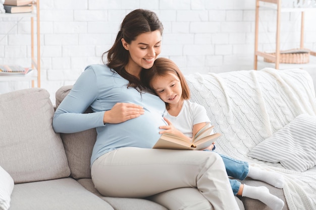 Happy family pregnant mother and preschooler daughter spending time together at home, reading book