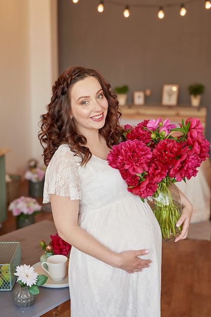 Happy family, pregnant woman in kitchen with peonies flowers. Motherhood, pregnancy, happiness concept. Girl with bouquet. Bouquet of peonies. Spring girl with flower