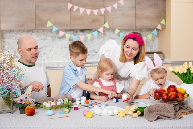 Happy Family preparing for Easter Cute children painting eggs Home activity Concept of unity and love Mom dad son daughter Brothers and sister