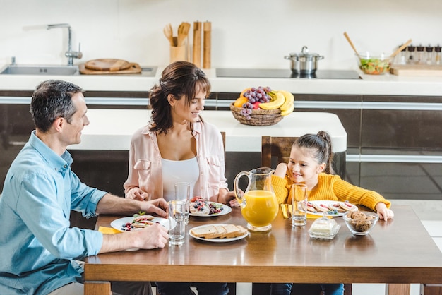 happy family sitting at table with juice and pancakes with berries at kitchen