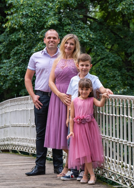 happy family standing on a white bridge in park Mom and girl are dressed in beautiful pink dresses