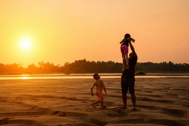 Happy family of three people, father, son and daughter on the beach at sunset sky