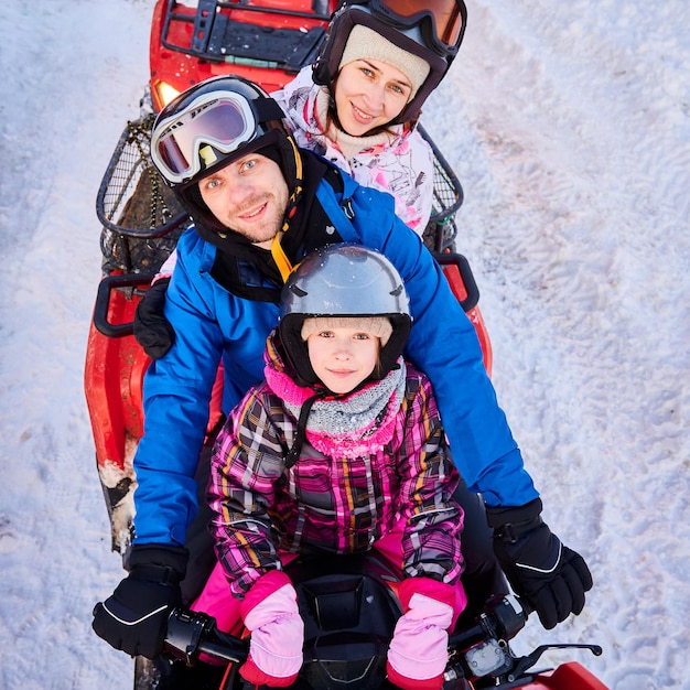 Happy family of three spending great time together in the mountains in winter riding quad bike