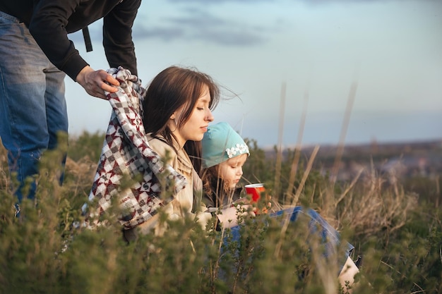 Happy family of travelers man covers with a blanket and hugs his wife and daughter in nature