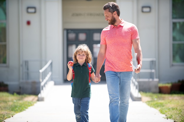 Happy family value. childhood and fatherthood. parent leads little child boy in first grade. nerd with teacher with book and apple. education. first day at school. father and son come back from school