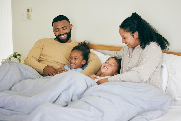 Happy family wake up and playing in bed in the morning bond and having fun in their home together Love bedroom and parents with children and tickle game and laugh play and cuddle on the weekend