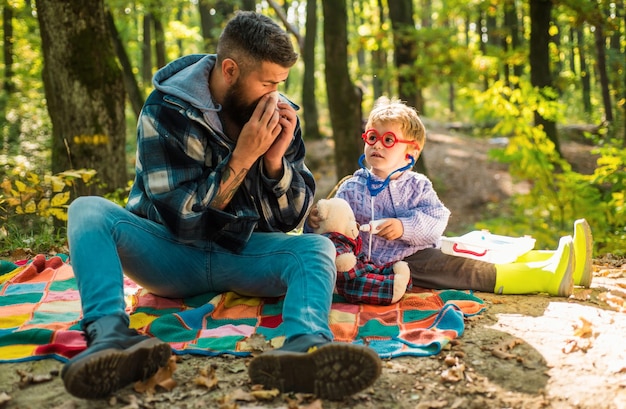 Happy family walking at autumnal park bearded dad catched a cold and sneeze at napkin father play