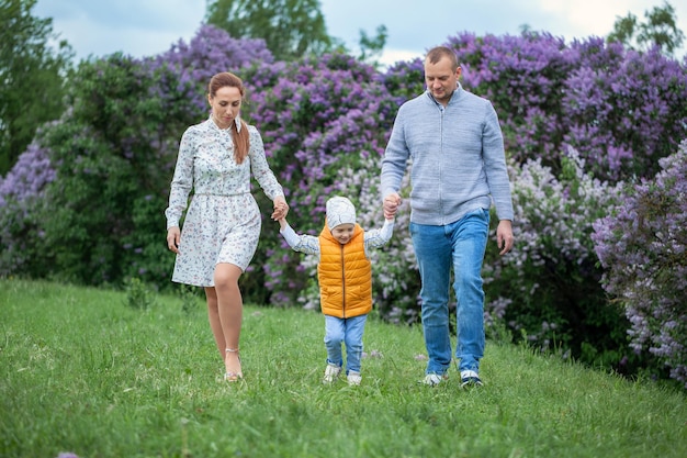 Happy family walking in the beautiful park. Parents holding the child's hands. Mom, dad and baby are happy to walk in summer day. Happy family concept.