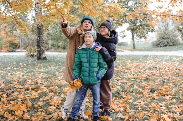 Happy family walking in sunny park and throws orange maple leaves mother with kids enjoying autumn weather outdoors