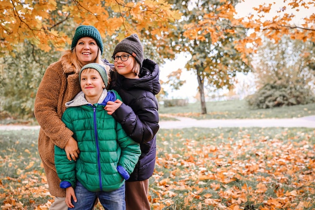 Happy family walking in sunny park and throws orange maple leaves mother with kids enjoying autumn weather outdoors