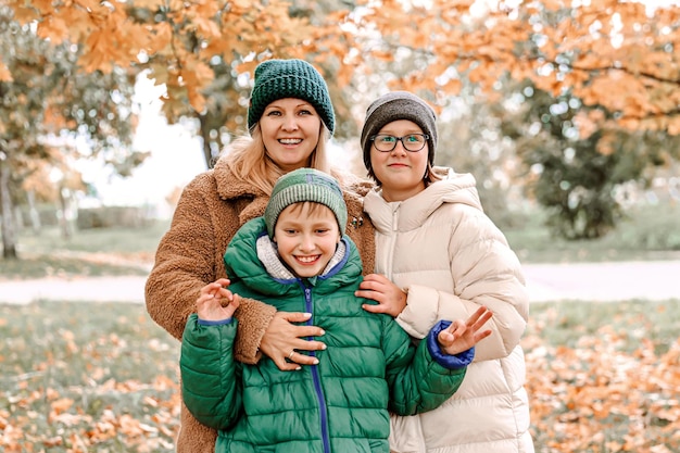 Happy family walking in sunny park and throws orange maple leaves mother with kids enjoying autumn weather outdoors