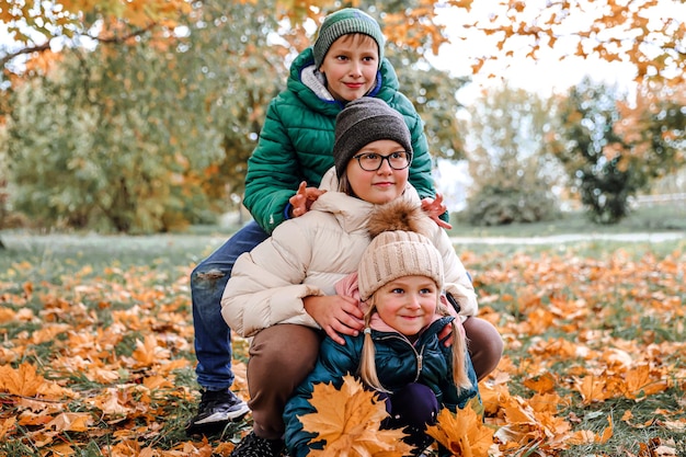 Happy family walking in sunny park and throws orange maple leaves mother with kids enjoying autumn weather outdoors