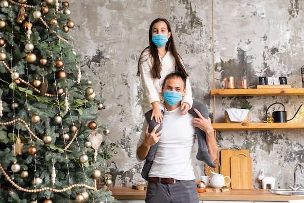 A happy family wear medical masks due to the COVID-19 coronavirus near Christmas tree. Xmas holidays.