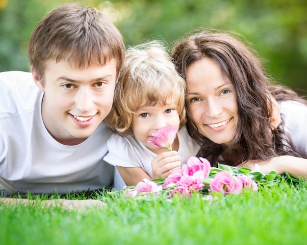 Happy family with bouquet of flowers lying on green grass outdoors in spring park Mothers day celebration concept