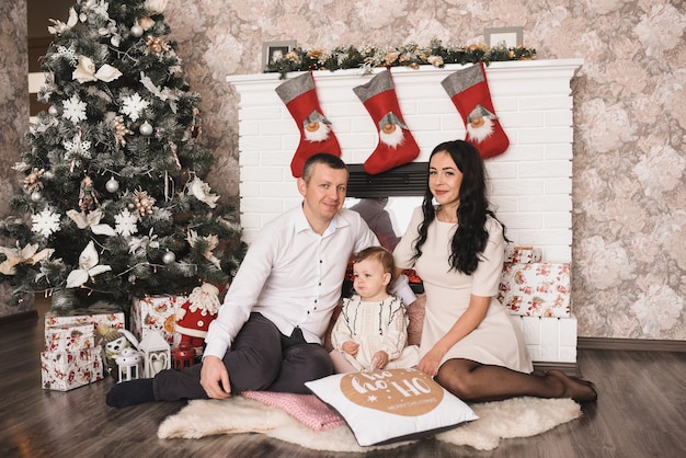 Happy family with child celebrating New Year and Christmas at decorated Christmas tree and garlands