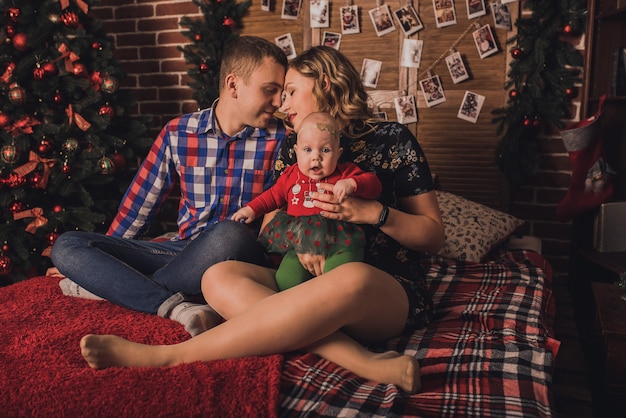 Happy family with child celebrating New Year and Christmas at decorated Christmas tree and garlands