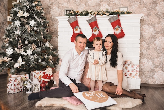 Happy family with child celebrating New Year and Christmas at decorated Christmas tree and garlands