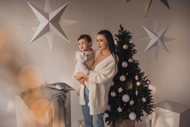 Happy family with child celebrating New Year and Christmas at decorated Christmas tree and garlands