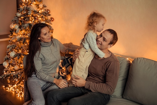 Happy family with a child at home near the Christmas tree are waiting for the New Year