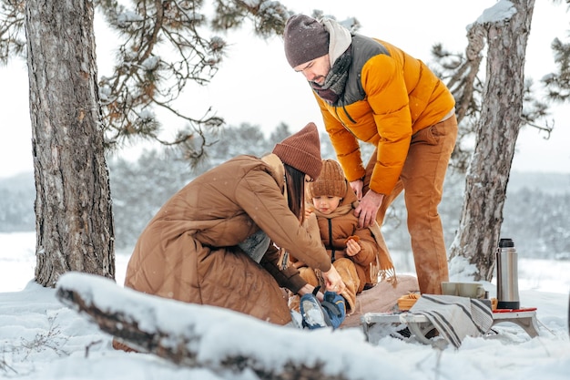 Happy family with cups of hot tea spending time together in winter forest