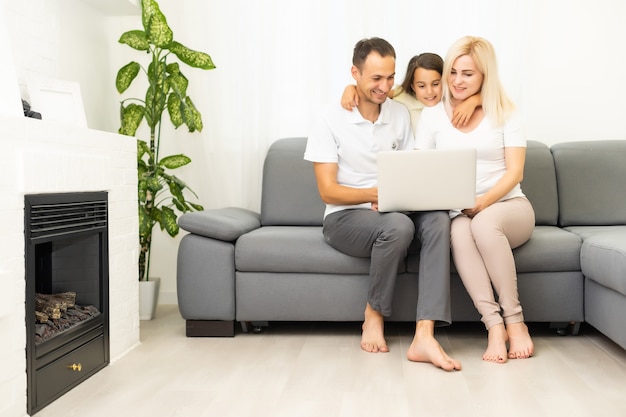 Happy family with kid girl having fun using laptop together sitting on sofa, parents and child daughter laughing relaxing at home with computer watching funny internet video, making online call