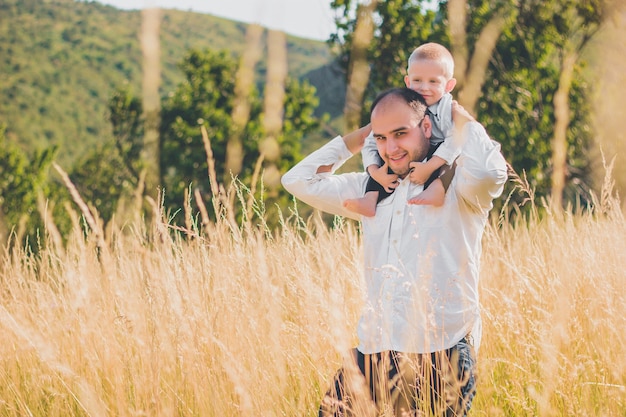 Happy family with kid walking together in wheat field on warm and sunny summer day. Soft focus.