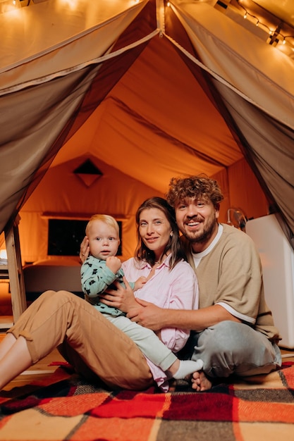 Happy family with lovely baby playing and spend time together in glamping on summer evening Luxury camping tent for outdoor recreation and recreation Lifestyle concept