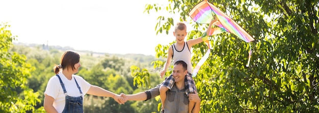 Happy family with pregnant wife fly a kite together in summer field