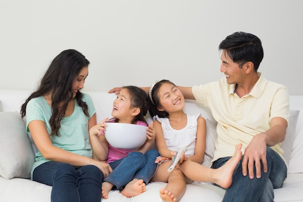 Happy family of with remote control and bowl on sofa in living room