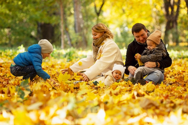 Happy family with three young children in an autumn park on a sunny day. The golden time of the year for walks and outdoor recreation. Love and tenderness.