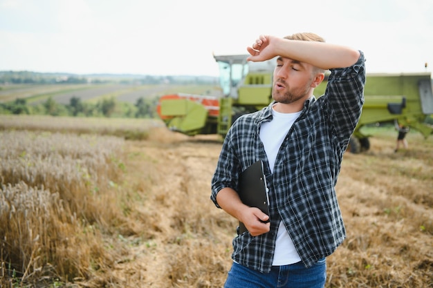 Happy farmer proudly standing in a field Combine harvester driver going to crop rich wheat harvest Agronomist wearing flannel shirt looking at camera on a farmland