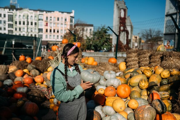 Happy farmer woman in a denim jumpsuit holds ripe pumpkin