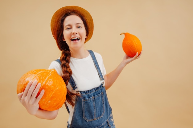 Happy farmer woman enjoys organic vegetables of ripe pumpkins on a beige background