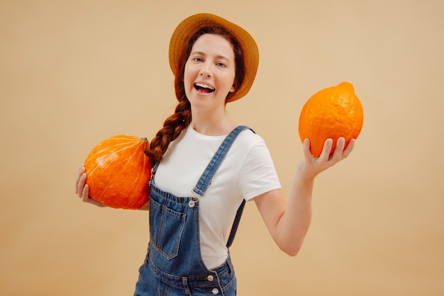 Happy farmer woman in overalls shows fresh autumn harvest of organic pumpkins on yellow background