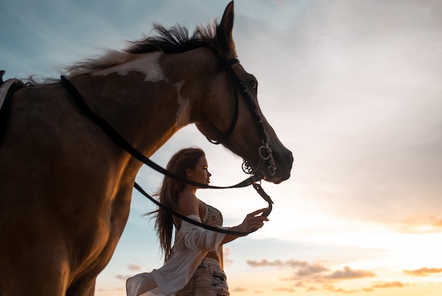 Happy fashionable young woman posing with a horse on the beach