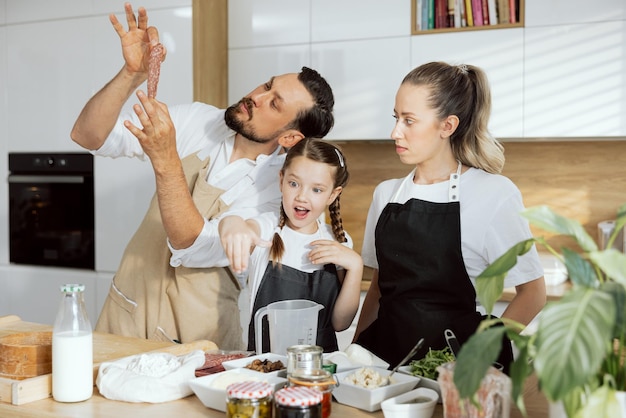 Happy father in aprons showing dellicious salami for mother