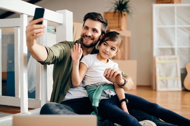 Happy father and daughter making video call over mobile phone at their new apartment