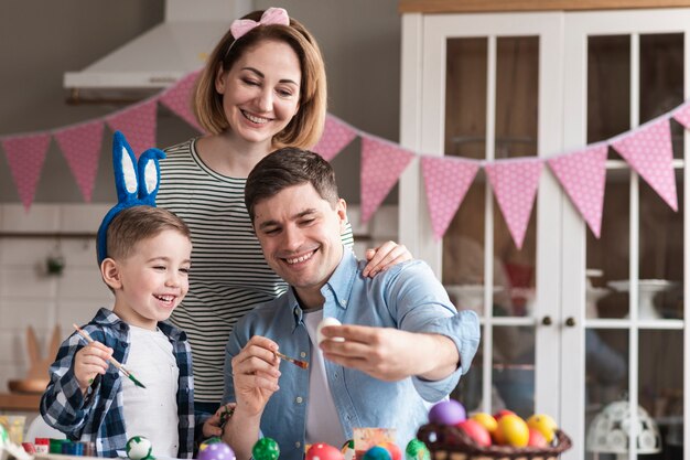 Photo happy father and mother painting eggs with child