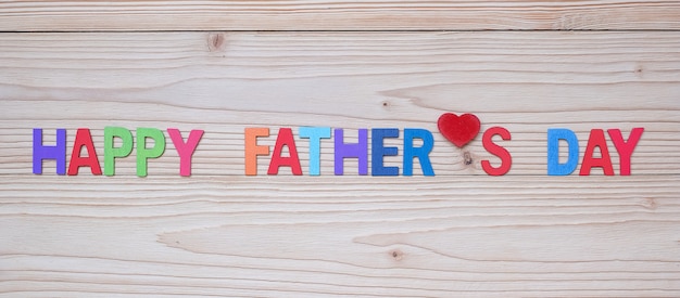 Happy Father's Day text with red heart shape on wooden background. 