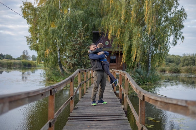 Happy father and son hugging and playing together in green nature Fisherman's house with a wooden pedestrian bridge on a tiny island in the middle of the lake