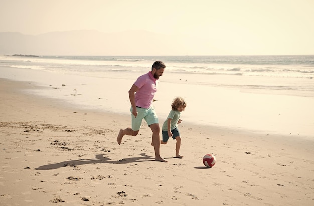 Happy father and son playing football having fun on summer sandy beach family vacation summer