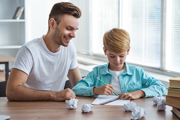 Photo the happy father and a son sitting at the desk and drawing on the paper