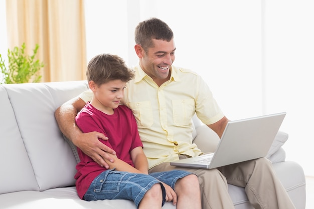 Happy father and son using laptop on sofa