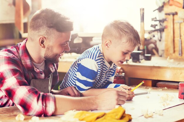 Photo happy father and son with blueprint at workshop