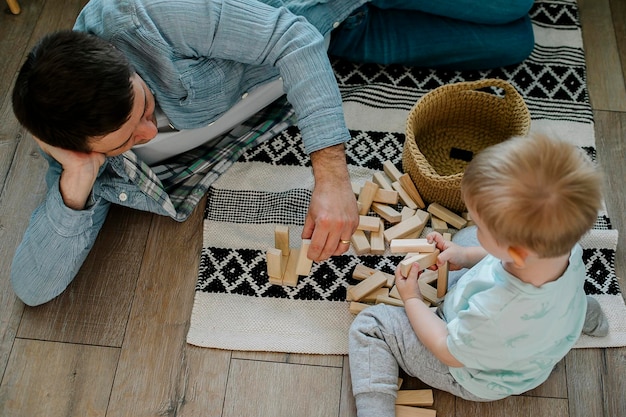 Happy father and toddler boy child little son playing with wooden blocks in children room at home