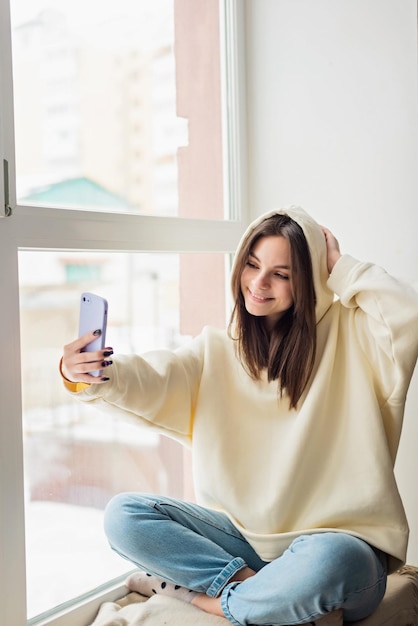 Happy female blogger taking selfie portrait on smartphone camera for social media posting cheerful teenage girl talking on video call with family or friends via mobile phoneSoft selective focus