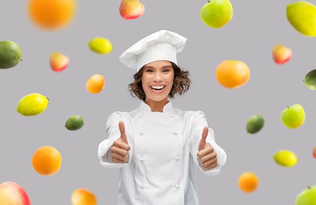 happy female chef showing thumbs up over fruits