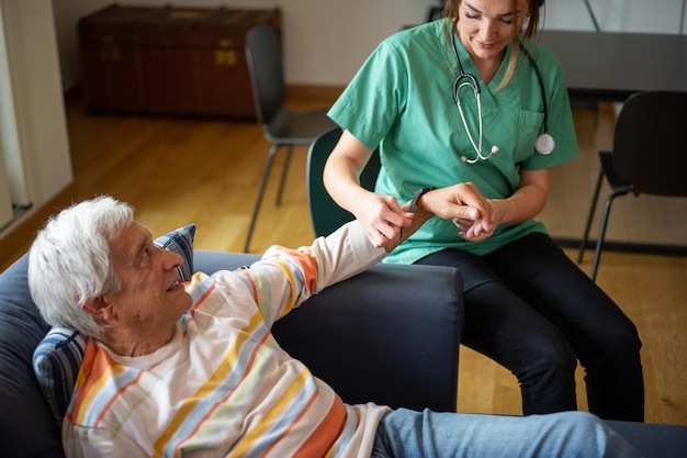 Happy female nurse with a stethoscope visiting an elderly man domestic medical assistant concept female doctor of the medical health system putting a smartwatch on a old man